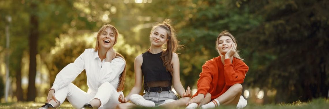 Three friends sitting on grass, enjoying a sunny outdoor day in the park.